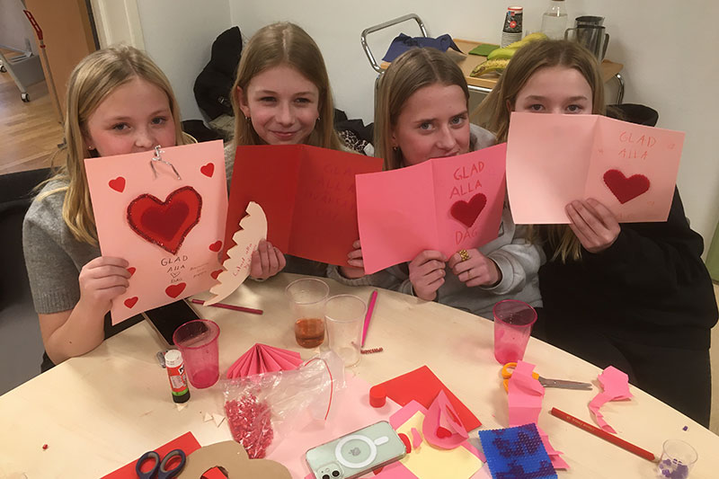 Fyra tjejer håller upp Alla hjärtan dags-kort framför sina ansikten.