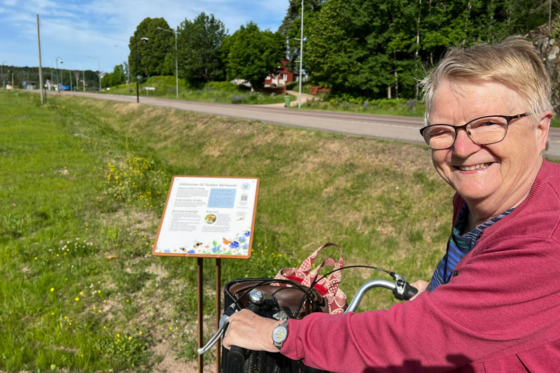 En glad kvinna med cykel. Informationsskylt bredvid.