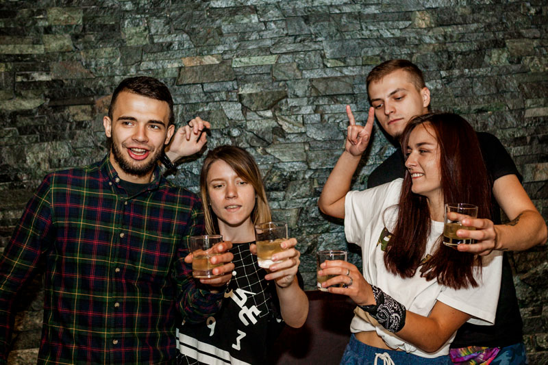 Mur i bakgrunden, framför står fyra personer med drinkar i händerna