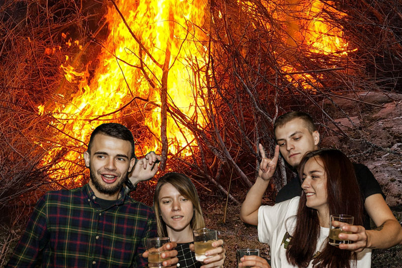Eldflammor i bakgrunden, framför står fyra personer med drinkar i händerna
